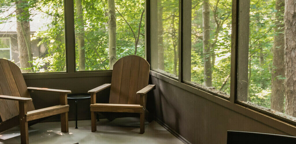 Two aerodeck chairs sit in the corner of a Hocking Hills State Park cabin's deck. Through the screens you can see a lush green forrest.  